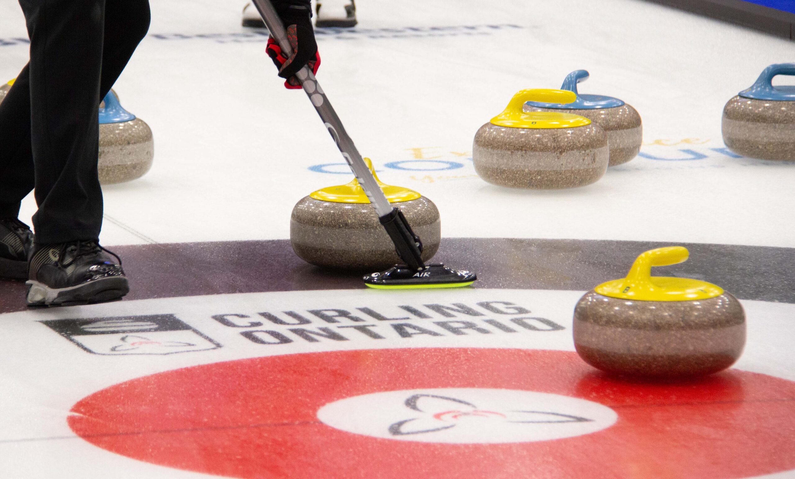curler sweeping a yellow curling rock into the rings with the curling ontario logo in the ice