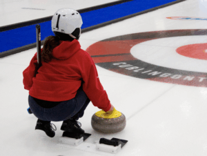 image of younth curler wearing a helmet sitting in the hack with a rock in hand