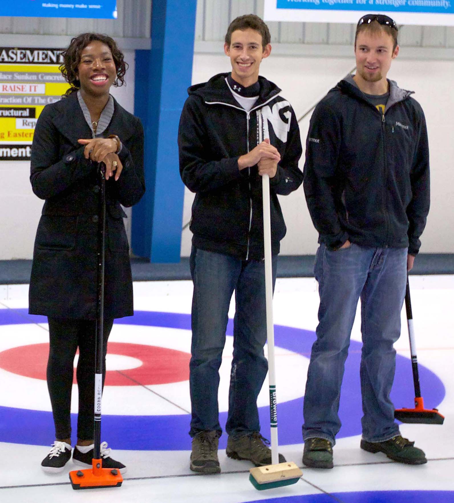 Image of three new curlers standing on the ice with brooms in their hand.