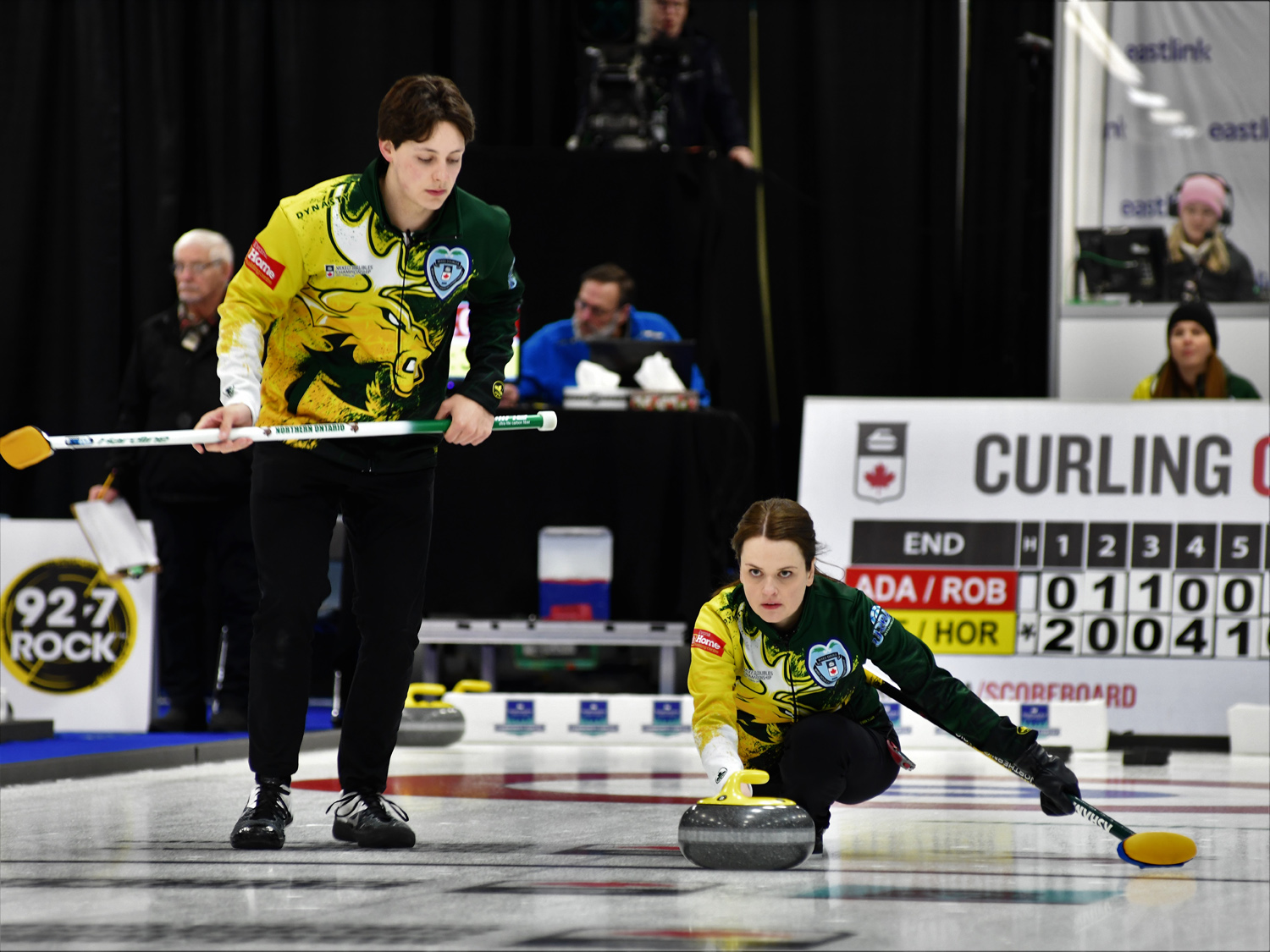 Northern Ontario Mixed Doubles team playing at nationals, female player sliding out with the rock and male player sweeping