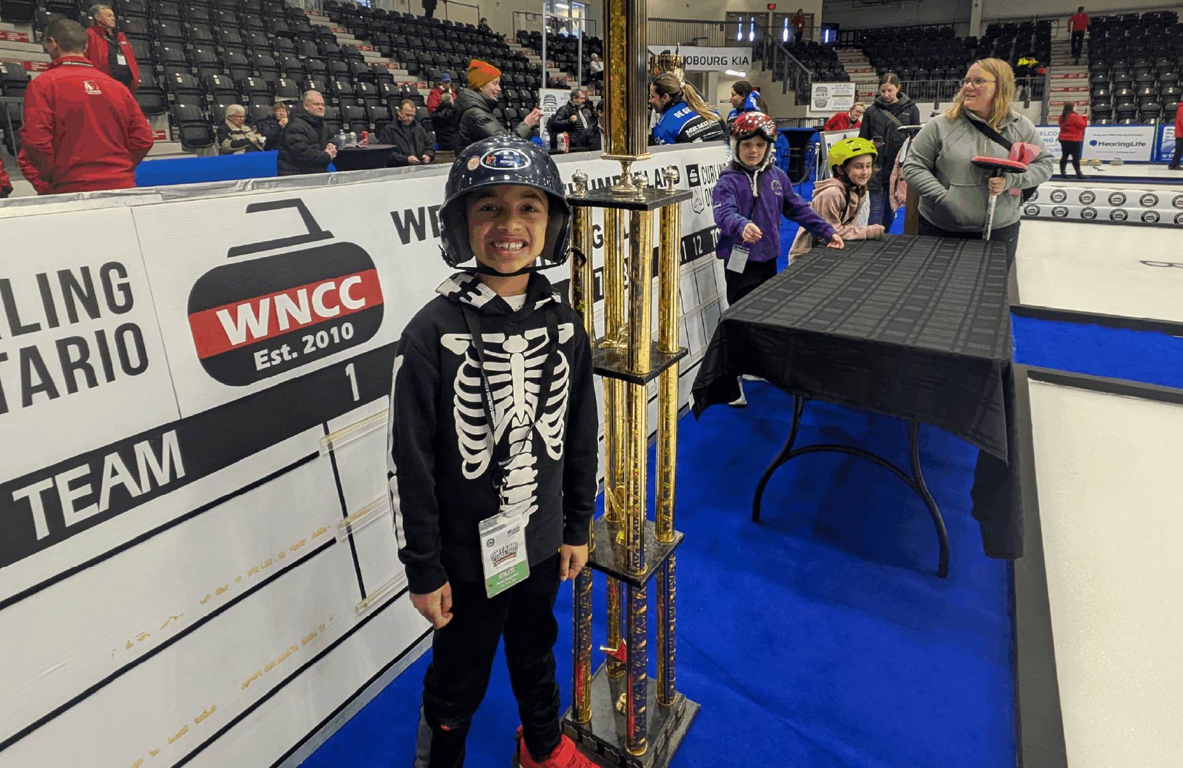 Young curler standing with the Hit Draw Tap Trophy that is taller than him!