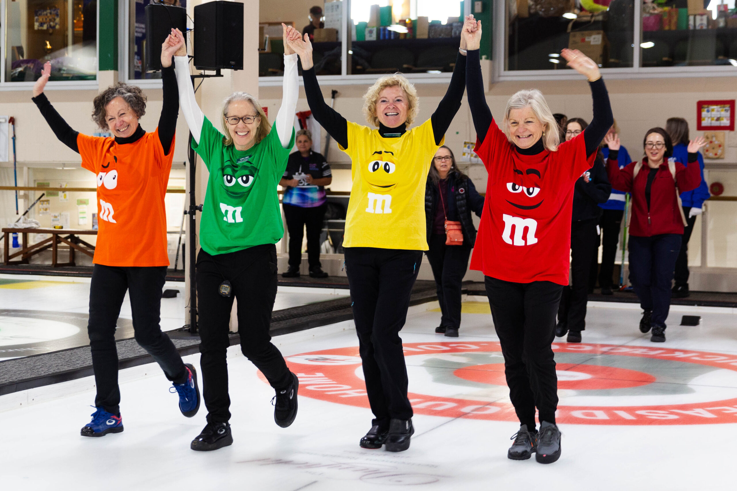 Women celebrating with their hands up at the Toronto Hope Bonspiel wearing M&M's t-shirts.